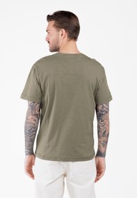 T-shirt w oliwkowym kolorze, z krótkimi rękawami, zaokrąglonym dekoltem i prostokątnym detalem na plecach. Wykonany z miękkiego materiału, o luźnym kroju.
