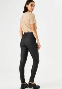 Jeans ajustados negros de cintura alta con una textura suave, bolsillos traseros y un diseño entallado, combinados con una camiseta de color beige claro.