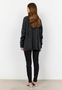 Overmaatse donkergrijze trui met lange mouwen, geribde manchetten en een hoge-lage zoom, gecombineerd met zwarte slim-fit broek en zilveren slidesandalen.