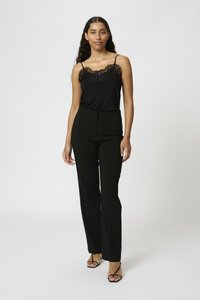 Camisola nera con bordo in pizzo abbinata a pantaloni neri a vita alta. La modella indossa sandali neri con cinturini. Materiale liscio, design aderente.
