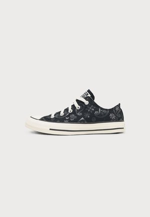 Zapatilla negra de corte bajo con suela y cordones blancos, con un diseño floral y paisley y un logo en la lengüeta.