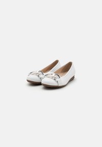 Ballerines blanches en cuir lisse, avec un nœud métallique argenté sur le bout et une semelle en caoutchouc texturé marron.