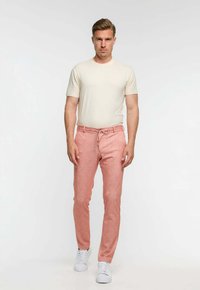 Ljusbeige kortärmad skjorta kombinerad med rosa texturerade byxor och vita sneakers. Outfiten har en avslappnad, figurnära design.