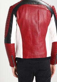 Leren jack met een rode rug, witte zijkanten en zwarte accenten. Geribbelde textuur op de mouwen en ritsen bij de manchetten, aansluitend ontwerp.