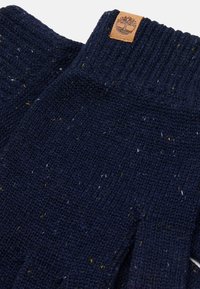 Navy pletené rukavice s žlutými a bílými fleky. Mají žebrovaný lem a hnědou koženou nášivku s logem stromu. Měkká textura a teplý design.