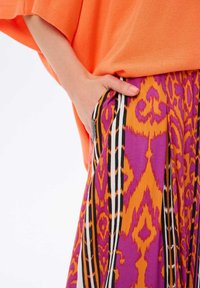 Jasnopomarańczowy sweter z dzianiny w połączeniu z wzorzystą spódnicą w kolorach fioletowym, pomarańczowym i czarnym. Spódnica ma plisy i boczne kieszenie.