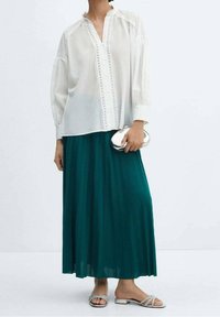 Witte blouse met geborduurde details en een geplooide, teal maxi rok. Gecombineerd met zilveren platte sandalen en een kleine metallic clutch.