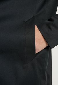 Giacca nera su misura caratterizzata da una trama tessuta, tasca laterale e linee pulite, che accentuano un design strutturato.