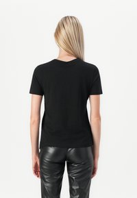 Black short-sleeve t-shirt made of soft cotton, featuring a round neckline and a relaxed fit, paired with sleek black faux leather pants.