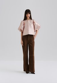 Rosa gemusterte Bluse mit Puffärmeln und rundem Ausschnitt, kombiniert mit braunen, weiten Suede-Hosen. Schlanker Schnitt mit unauffälliger Oberfläche.