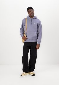 Hoodie gris en mélange de coton avec une poche kangourou à l'avant et une capuche à cordon de serrage, associé à un pantalon large noir et des baskets beiges.