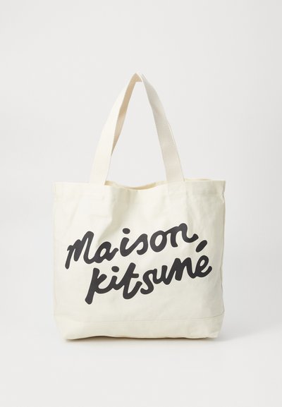 Plátěná taška v krémové barvě s černým nápisem "maison, kitsuné." Obsahuje pevné uši a jednoduchý design.