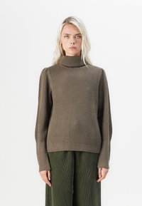 Brun ribbad polotröja med långa ärmar, med en avslappnad passform och textilstruktur. Buren tillsammans med gröna kordflorsbyxor med vida ben.