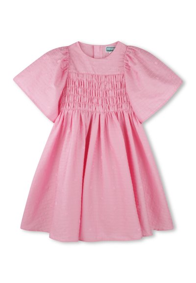 Robe rose avec des manches courtes bouffantes, présentant des détails de corsage smocké et un tissu texturé avec des motifs subtils. Fermeture à boutons au dos.