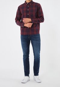 Červená a námořnická pruhovaná košile na knoflíky, bavlněný materiál, dlouhé rukávy, spárovaná s tmavě modrými slim-fit džíny a bílými teniskami.
