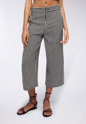 Pantaloni cropped a righe bianche e nere con chiusura a bottone, caratterizzati da una vita alta e una vestibilità ampia. Abbinati a sandali neri con cinturini.