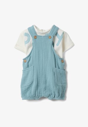 Combinaison bébé bleu clair texturée avec boutons en bois et poches avant, portée sur un t-shirt blanc à manches courtes avec inscriptions bleues.