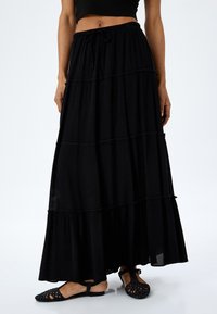 Falda maxi negra en capas con cinturilla el�ástica y cordón. Fabricada con tejido ligero, presenta un diseño fluido y un acabado texturizado.