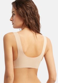 Sujeción beige sin costuras con tirantes anchos y una textura suave. Presenta un escote redondeado y una parte posterior baja, ofreciendo un diseño minimalista.
