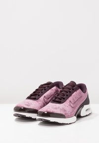 Scarpe Nike con tomaia in suede rosa e viola, lacci neri e una suola intermedia bianca con un dettaglio sul tallone in nero lucido.