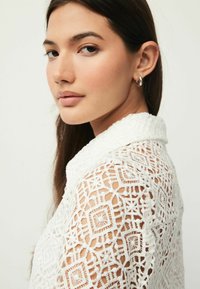 Valkoinen brodeerattu paita, jossa on monimutkaisia lace-kuvioita, kaulus ja lyhyet hihat, sileä pinta ja hienostuneet yksityiskohdat.