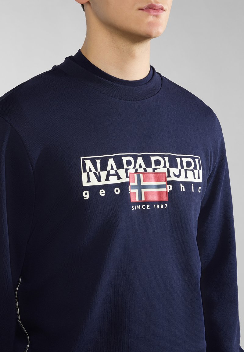 Marineblaues Langarmshirt aus Baumwolle, mit weißem und rotem Logo-Text sowie einem Patch mit der norwegischen Flagge. Glatte Textur, runder Ausschnitt.