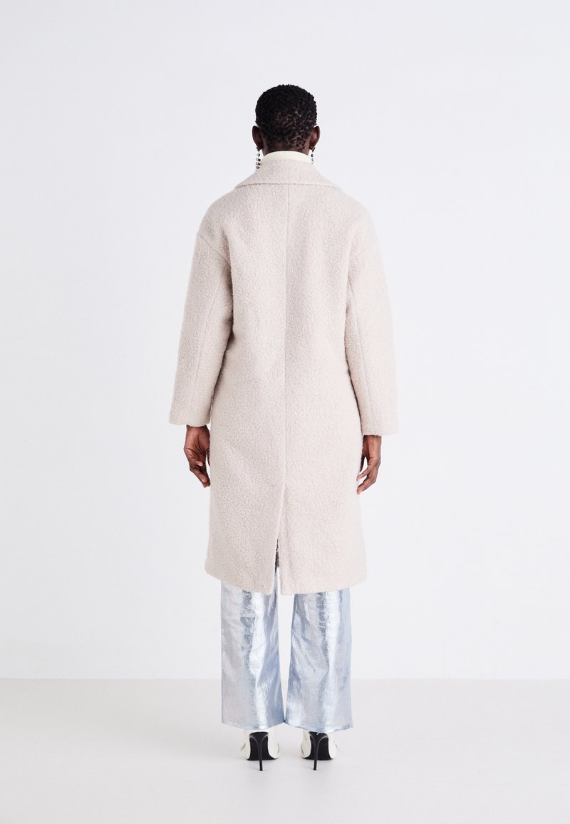 Beiger strukturierter Übermantel mit geradem Schnitt, Schalkragen und mittigem Rücken-Schlitz, kombiniert mit glänzenden silbernen weit geschnittenen Hosen und High Heels.