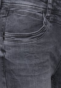 Primer plano de unos jeans de mezclilla negros desgastados que muestran el bolsillo delantero y la costura detallada.