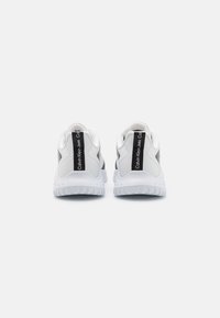 Valged sneakers tekstuuriga viimistlusega, millel on must bränditud silt taga ja pehme tallaga toetuseks ja mugavuseks.