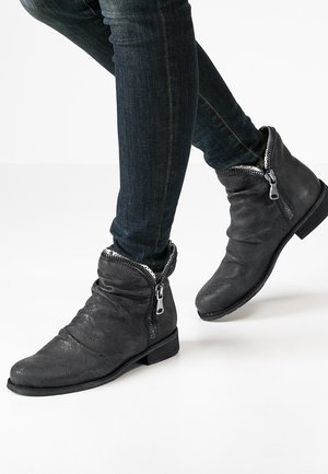 Black leather ankle boots with textured surface, zip closures, and folded cuffs, paired with dark jeans. Flat sole and minimal detailing.