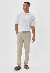 Vit bomullströja, beige byxor med dragsko och mörka sandaler. Enkelt design, avslappnad passform, med en mjuk textur och inga synliga mönster.
