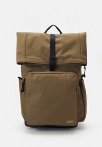 Mochila de tela color marrón claro con diseño de rollo en la parte superior, bolsillo frontal, detalles en negro, correas laterales y asa en la parte superior. Cuenta con una superficie duradera y texturizada.