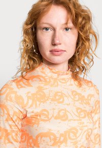 Top de manga longa e gola alta em pêssego com padrões abstratos em laranja. Textura suave, material elástico, design ajustado.