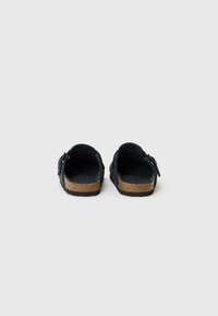 Black felt clogs with a cork sole, featuring adjustable buckles and an open back, displaying a textured upper and smooth lip.