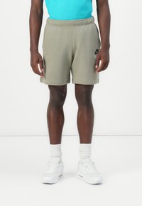 Grønne bomullstreningsshorts med elastisk midje, lommer på siden og Nike-logo på venstre lår. Kombinert med hvite joggesko og sokker.
