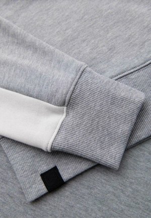 Lichtgrijze sweatshirt met een geribde manchette en een witte accent. De stof heeft een zachte textuur en een subtiel gemêleerd patroon. Zwarte logo-tag zichtbaar.