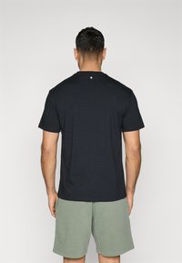 Black short-sleeve t-shirt with crew neck, featuring a small logo detail near the collar, paired with olive green shorts.