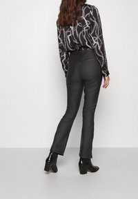 Czarne dzwony o gładkim, teksturowanym wykończeniu, zestawione z bluzką w czarno-białym wzór łańcucha oraz czarnymi botkami na słupku.