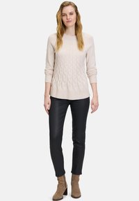 Světle béžový svetr s pleteným vzorem a kulatým výstřihem, s žebrovanými manžetami, v kombinaci s černými slim-fit kalhotami a hnědými kotníkovými botami.