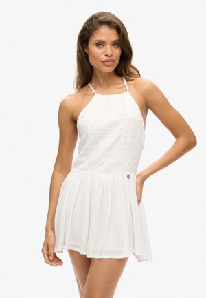 Witte zonjurk met een halternek ontwerp, een gestructureerde lijfje en een vloeiende rok. Heeft een getailleerde taille en subtiele knoopdetails aan de zijkant.