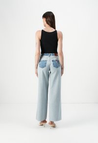Light blue wide-leg jeans with contrasting denim patch back pockets, paired with a black ribbed tank top and beige high heels.