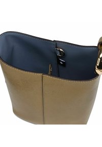 Borsa a secchiello in pelle beige con morbido rivestimento interno blu, accessori in oro e una piccola etichetta nera all'interno.