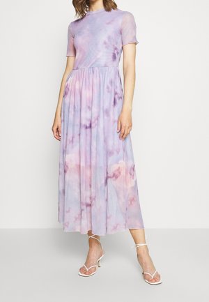 Femme portant une robe midi tie-dye pastel violet et rose avec manches courtes et sandales blanches à talons avec lanières.