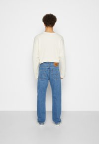 Lichte crèmekleurige geribbelde trui gecombineerd met blauwe rechte broek met een bruin lederen label en achterzakken met een witte merklogo.