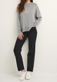 Maglione grigio in maglia con scollo rotondo, abbinato a jeans neri a gamba dritta e sneakers bianche. Il maglione presenta spacchi laterali sull'orlo.