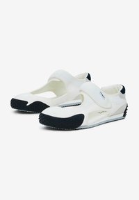 Des chaussures blanches avec un design en maille respirante, une sangle Velcro et une semelle en caoutchouc noir texturé dotée de renflements ronds pour une meilleure adhérence.