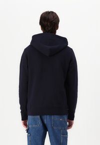 Felpa navy in morbido cotone con orlo a costine, cappuccio regolabile con coulisse e tasca a marsupio, mostrata da dietro.