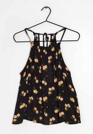 Schwarzes ärmelloses Kleid mit gelbem und weißem Blumenmuster, mit Bindebändern am Rücken, hängend an einem schwarzen Drahtbügel vor weißem Hintergrund.