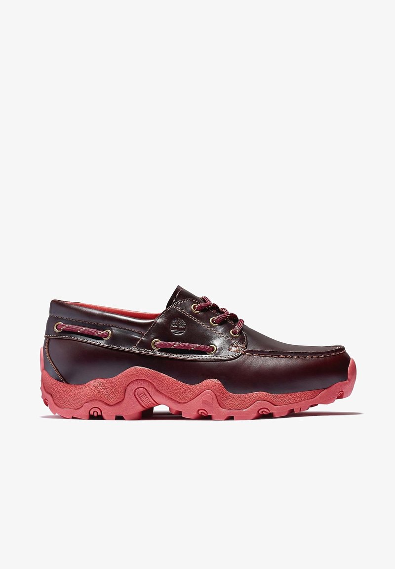 Chaussures bateau en cuir marron avec semelles en caoutchouc roses, dotées de lacets et de coutures contrastants, et d'un design à bout arrondi.