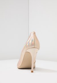 Lodička na vysokém podpatku z iridescentního materiálu, s špičatou špičkou a hladkým, lesklým povrchem. Úzký béžový stiletto podpatek.